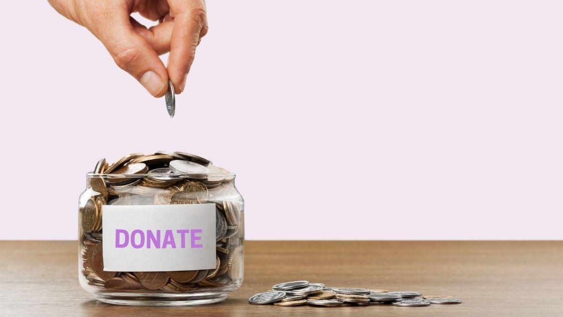 Hand dropping a coin to a donation jar with coins inside and outside scattered