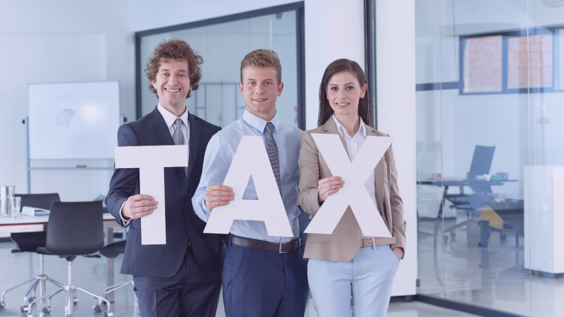 1 Three professionally dressed individuals standing in an office environment, smiling and holding large letters that spell out “TAX”—symbolizing tax-related matters, suitable for a blog about understanding or challenging SARS auto-assessments.