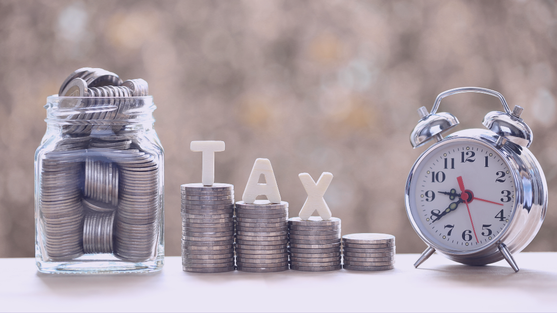 ON Q Blog Banner (1) Stacked coins spelling out "TAX" beside a jar of coins and a classic alarm clock, symbolizing the importance of saving money and managing time for tax planning.