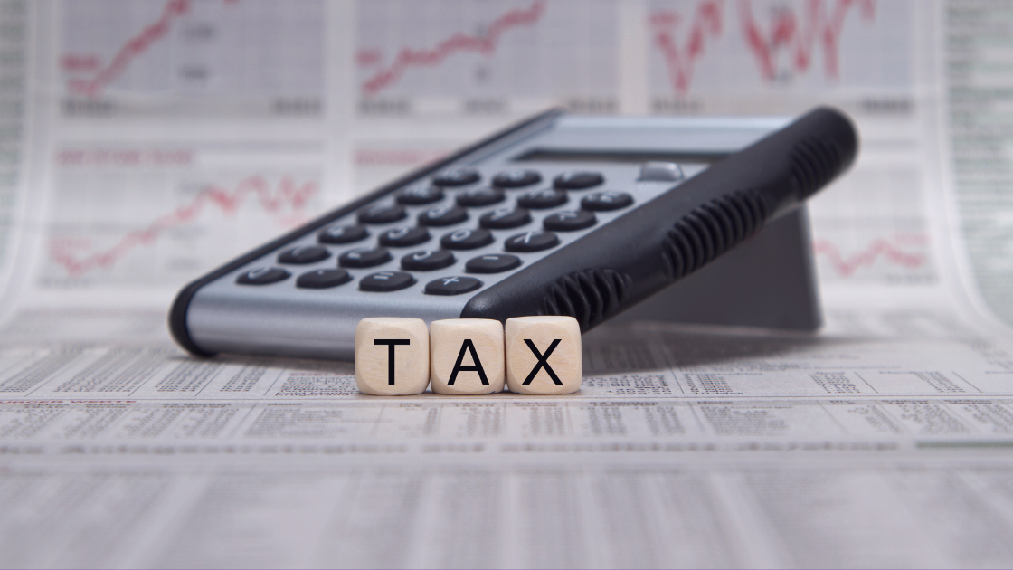 When Tax Transparency Isn’t Optional A close-up image of a calculator resting on financial newspapers, with three wooden blocks in front spelling out "TAX." Red line graphs are faintly visible in the background, suggesting financial analysis or tax calculations.