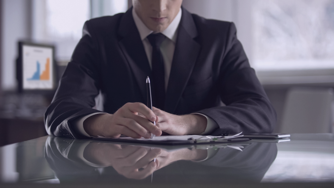 Why Company Directors Should Pay Themselves a Salary Business director in formal suit reviewing documents and preparing to sign papers at a desk.