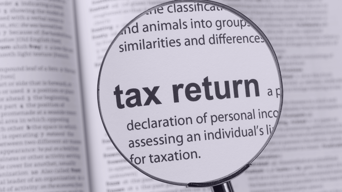 Why Sole Proprietors Must File Tax Returns — Even Below the Threshold A magnifying glass highlighting the words “tax return” on a printed page, symbolizing focus on tax filing requirements for sole proprietors.
